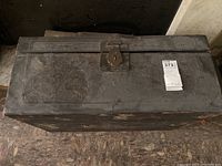 Top view of black chest showing overall rectangular shape with embossed floral pattern on surface and metal latch lock.