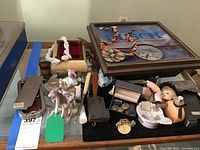 Wide shot showing the assortment including goat figurine with rider, doll parts, buttons, clock, and various small items on a table.