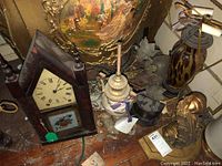 View of the clock, urn lamp, and decorative brass lamp parts on wooden surface showing damage and wear