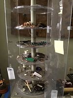 Multi-tier circular display stand with various vintage costume jewelry items including bracelets, earrings, hat pins, and eyeglasses.