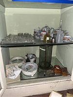 Mixed lot of ceramic tea cups and saucers, glass vase with metal frame, Goebel figurines, small decorative birds and butterflies, bells, and trays, overall shelving display