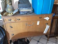Front view of wood dresser showing three drawers with metal handles and carved details. Scuffs and scratches visible on surface.