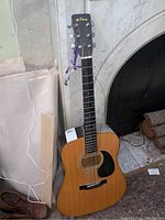 Full view of the M. Suzuki acoustic guitar standing upright showing the whole instrument including the body, neck, headstock, and one broken string.
