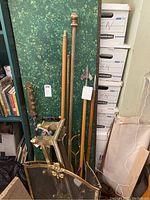 Photo showing wooden harpoon replicas, flag poles, walking cane, and broom leaning against a green backdrop near boxes and other items.