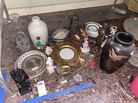 Overview of lot showing various plates, a white stoneware jug, decorative bowls, brass and crystal swan figurines, and other collectible figurines.