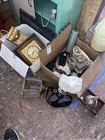 Full view of lot items in boxes and some on ground including clock, telephone, belts, lamps, sconce, handbag