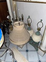 Photo showing multiple lamps including candelabra lamps and one lamp with beige shade, some lamps with candle-style light bulb holders.