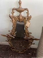 Front view of gold-colored ornate mirror with eagle decorations and urn design on top
