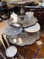 Three-tier wooden nesting tables with scalloped edges and turned pedestal support, showing wear and dust.