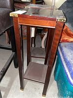 Full view of wooden plant stand showing brass corner accents and tall, slender legs.