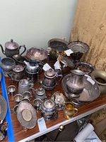 Wide view showing multiple silver plate items including tea pots, bowls, plates, basket, candlestick holder, and vases on a table.