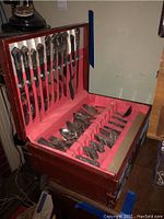 Open wood box displaying full silver plated flatware set against pink velvet lining.