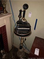 Photo showing a black rotary phone sitting on top of a miniature black toy piano; both are placed on the marble plant stand's top.