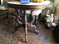 Full view of the antique round wooden table with marble top and casters, showing detailed legs and wear.