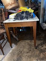 Full view of the rectangular wood table with white marble top and four tapered legs with caster wheels, showing scratches and wear.