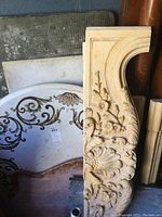 Photo showing three decorative pieces: circular tabletop with painted scroll and floral design, and two carved panels with floral and shell motifs