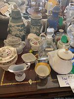 Overview of the lot showing vases, jars, teapot, teacup, and decanter arranged on a wooden table in an indoor setting.