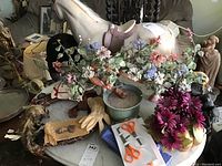 Photo showing the lot items arranged on a round table, including the faux bonsai tree, gloves, button wreath, feathers, horse figurine, headpiece, and artificial flowers.