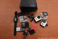 Showing full lot of 2 Soocoo 5200 action cameras, 2 white GoPro Hero3 cameras, wrist remote, multiple batteries, mounts and a hard case.