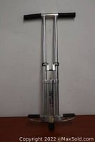 Front view of the aluminum pogo stick with black foam grips and foot pedals against a plain background