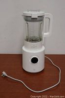 Full view of white blender with glass jar and power cord with regional plug.