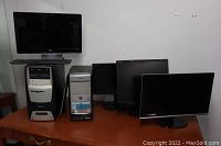 Photo showing four monitors, two desktop towers, and one keyboard arranged on a wooden table.