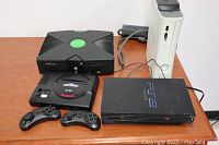 Overview of four gaming consoles: original Xbox, Sega Genesis Mini with controllers, PS2, and Xbox 360