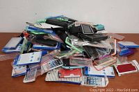 Pile of assorted phone and tablet cases including some sealed in packaging, shown stacked on a table.