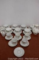 Photo showing full matching tea set including cups, saucers, pot, cream and sugar dispensers on wooden table