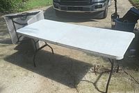 Two folding tables, one set up and one folded, on concrete driveway with vehicle in background.