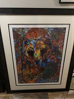 Photo of a framed abstract colorful painting of a bear's face with a black and white frame, showing details and colors