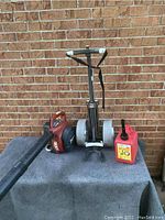 Full view of leaf blower, foldable golf caddy, and red gas can on a table