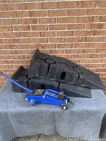 Car jack positioned beside stacked Rhino Ramps against a brick wall.