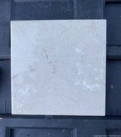 Photo of square beige ceramic floor tile with subtle texture seen against black background.