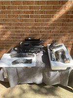 Photo of the gas logs and burner parts arranged on a surface outside against a brick backdrop, showing multiple charcoal-style ceramic log pieces and one metal burner component.