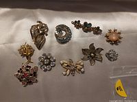 Photo showing ten assorted vintage pins including floral, star, crescent moon, sun, and insect motifs with various colored stones.