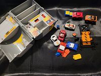 Fold-out oil can shaped garage playset with 7 miniature vehicles and various small accessories scattered around it on a black fabric background.