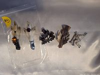 Five Scottish-themed pins arranged on white fabric, showing two grouse foot pins with fur and stones, two thistle pins, and one bagpiper pin.