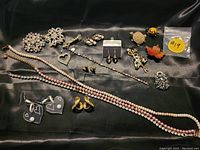 Full lot display of 5 pairs of earrings, 7 brooches, 3 necklaces including faux pearl strands, 1 bracelet and 1 pendant on dark fabric background.
