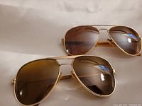 Two pairs of aviator sunglasses lying on a white surface, front view showing lenses and frames