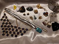 Full lot overview of the 3 necklaces, 6 pins, 2 pendants, 2 rings, 3 pairs of earrings and 1 wide bracelet laid out on a fabric background