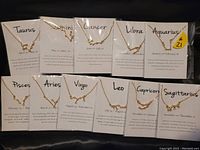 Eleven gold tone zodiac constellation necklaces displayed on cards showing zodiac names and date ranges.