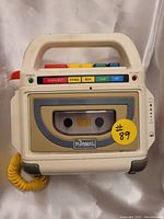 Front view of the Playskool tape player showing the cassette compartment with tape, colorful control buttons, and yellow coiled microphone.