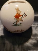 Close-up of Bunnykins character rabbit in orange jacket riding a hobby horse on the side of the ceramic coin bank.