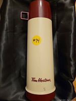 Photo of cream-colored Tim Hortons thermos with red logo and screw-on lid, placed on a black surface.