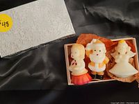 Three vintage Christmas candles in original box with tissue paper. Included are choir girl, angel, and Santa Claus shaped candles in white wax with painted details.