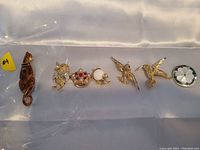 Seven vintage and retro pins displayed in a row on white fabric, showing diverse animal and decorative designs.