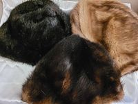 Three vintage fur hats in dark greenish-black, tan, and black with brown tones, showing soft plush fur exterior.