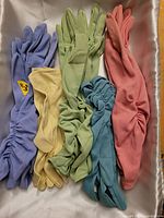 Six pairs of women's fashion gloves in different colors, all featuring ruched fabric detail, laid flat on a satin background.