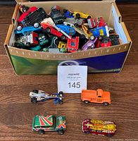 Box filled with assorted diecast vehicles including cars, trucks, and specialty cars with some visible decals and paint colors